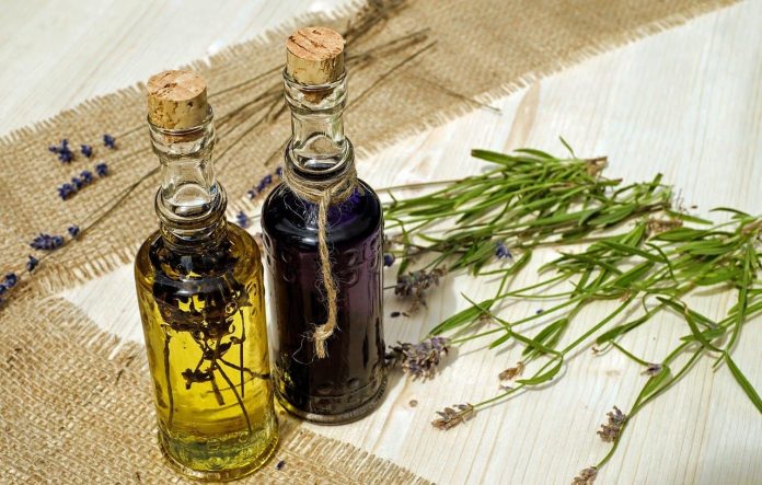 Two glass bottles with cork stoppers. One contains lavendar in oil and the other contains a purple liquid.