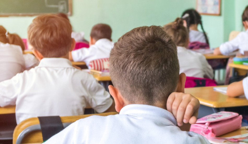 Group of school kids sitting and listening to the teacher in the classroom, as seen from the back of the room.