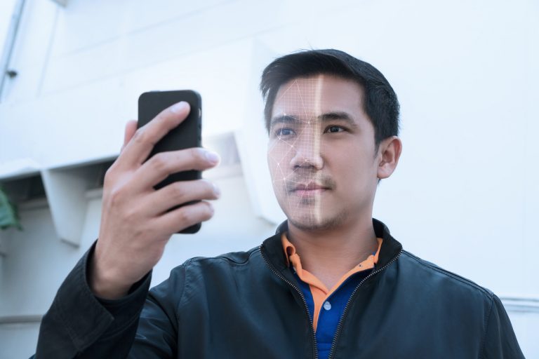 Asian man looking at phone with facial recognition.