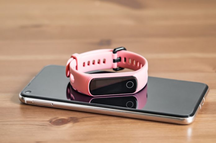A pink fitness tracker sitting atop a smartphone on a wooden table.