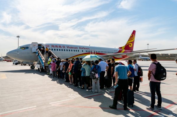 Passengers are standing in line on the tarmac waiting to board a Hainan Airlines plane.