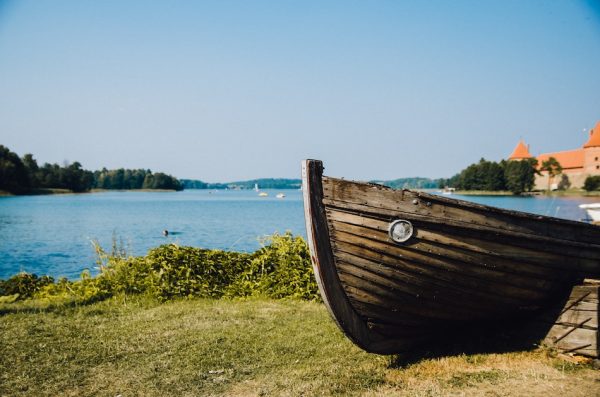 Lullaby country - image of a corner of a boat by a lake with an orange roof building far in the distance - photo of Trakai, Lithuania