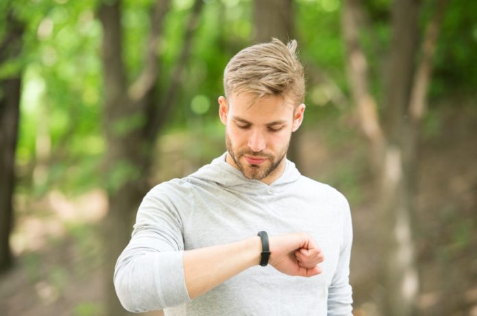 A young man in the woods checking his fitness tracker.