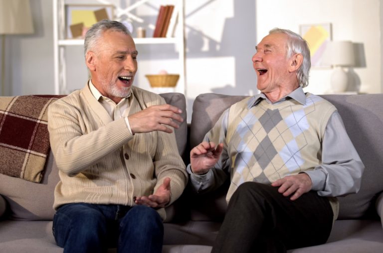 Aged brothers laughing while sitting on a sofa together.