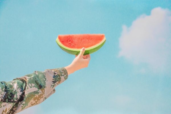 hand holding a slice of watermelon up highs blue sky background with white cloud