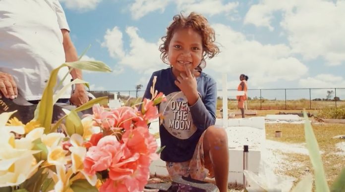 Aboriginal boy with fresh flowers by a grave smiling it is a bright and sunny day