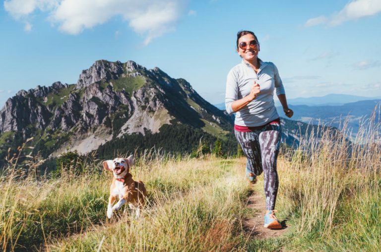 Happy smiling woman jogging on a mountain trail with her beagle.