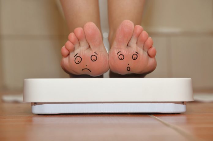 A woman tipped back on her heels to show the soles of her feet while standing on the bathroom scales.