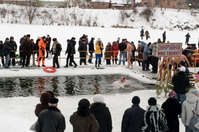 A group of people gathered outside in winter to watch as member of a swim club swim in a lake.
