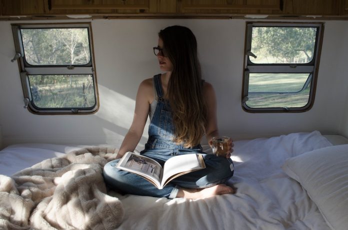 girl holds cup of tea as she sits on her bed in a caravan