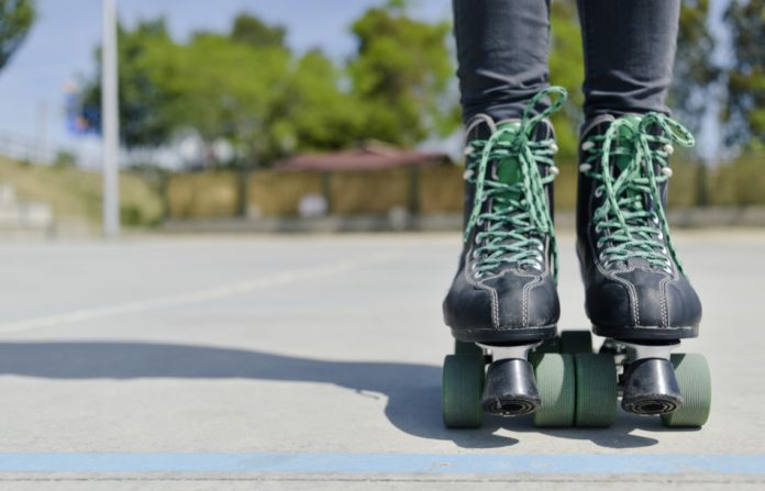 Close up of a young man's black roller skates with green wheels and matching laces.