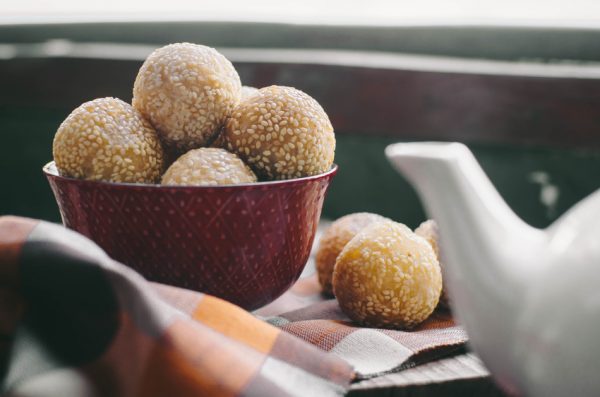 A bowl containing sesame balls sits beside a white porcelain teapot on a cloth napkin.