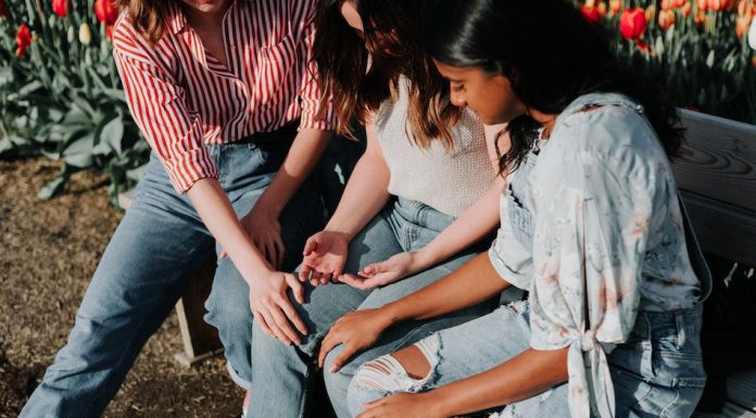 3 female friends sit on a bench the two girls on the outside rest hands on girl in the middle to support her through feelings of anxiety
