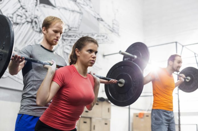 Coach at the gym helps a woman have proper form while lifting free weights.