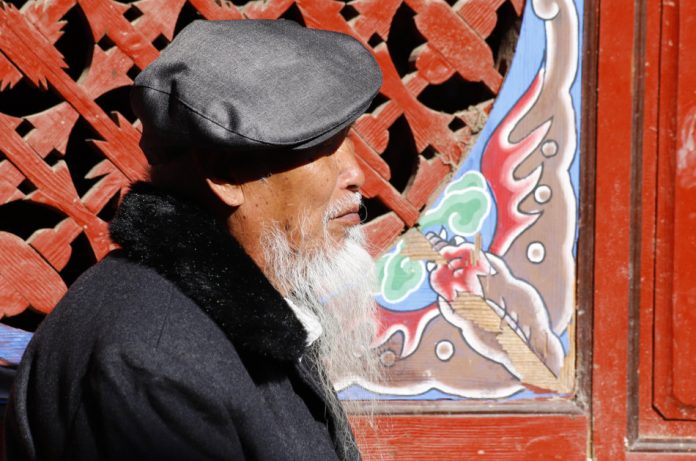 An elderly Chinese man with a characteristic beard walking along the street in the village of Shigu, Yunnan, China.