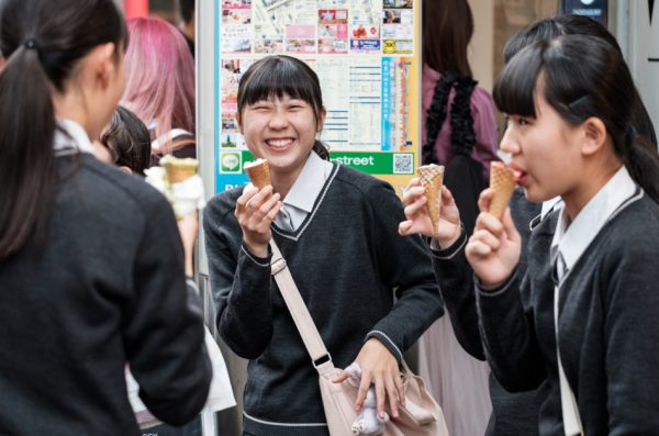 A laughing Japanese school girl with her friends, all in their school uniforms eating ice cream cones.