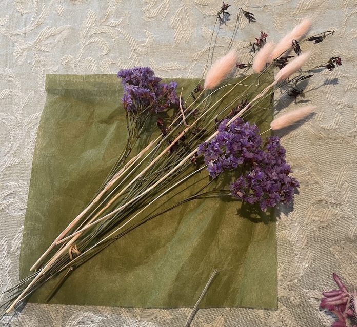 Dark green floral wrapping cut into a smaller square with Butterfly flowers then Bunny tails then the Perezii Blue and then added the Kangaroo Paw to fill the gaps and to lay in a balanced diamond shape also adding flowers with the shorter stems in the middle of the bouquet. Only the Whirling Pink Butterfly bush flowers are tied together for easier handling.