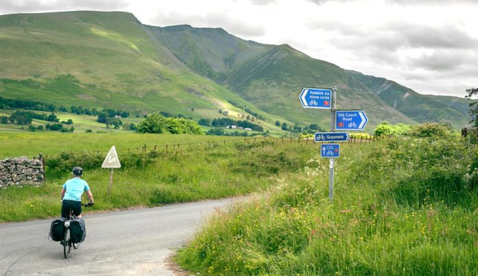 Lone cyclist riding the Coast to Coast C2C cycle route through the hills of the Lake District, Cumbria, UK.
