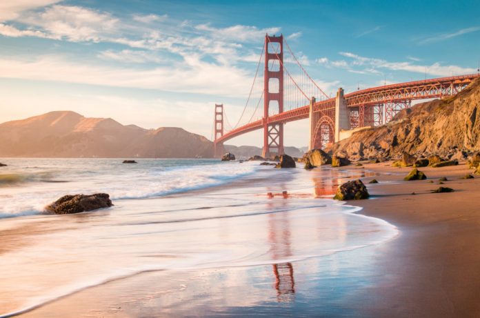 Classic panoramic view of famous Golden Gate Bridge seen from scenic Baker Beach in beautiful golden evening light on a sunny day with blue sky and clouds in summer, San Francisco, California, USA.