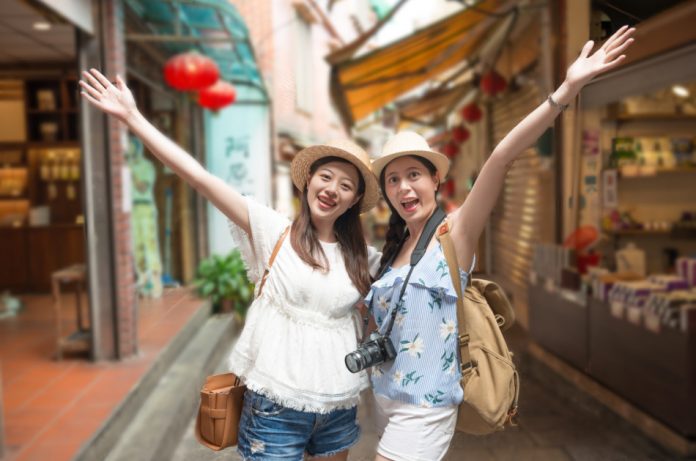 Two smiling Asian girls wearing hats pose for a picture in front of some shops while touring a mountain town in Taiwan.