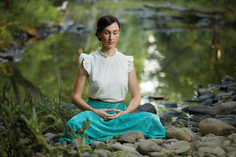 singer songwriter katy mantyk meditates Falun Dafa by a river she is sitting with legs folded and hands conjoined