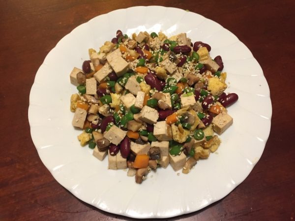 cooked vegetables and tofu and egg mixed on white plate with sesame seeds on top