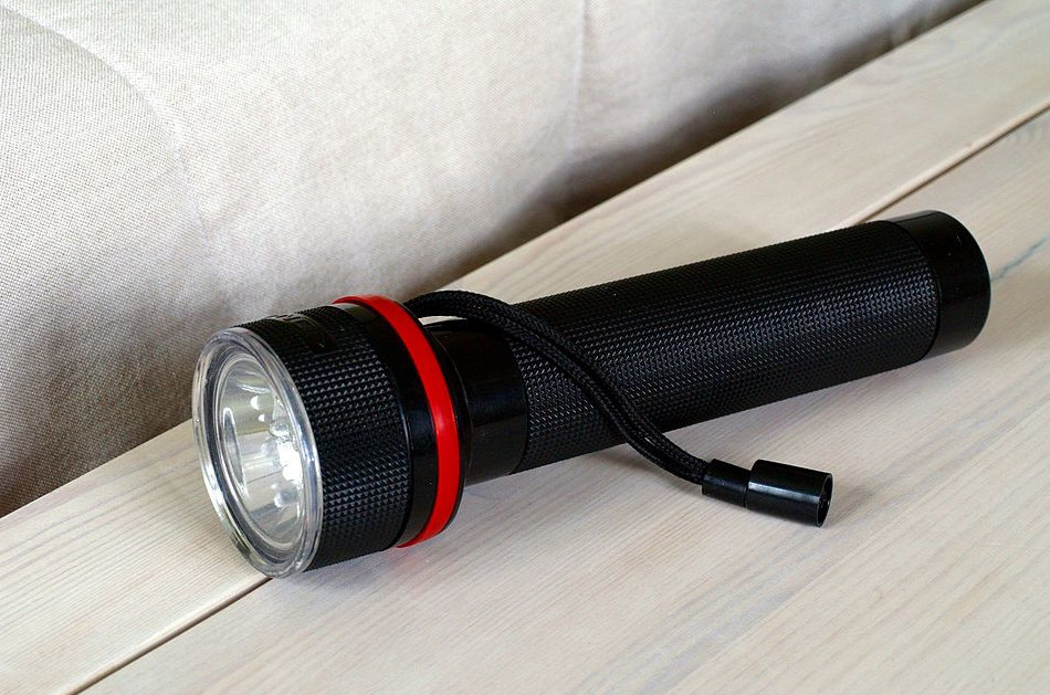 A black flashlight sits on a nightstand.