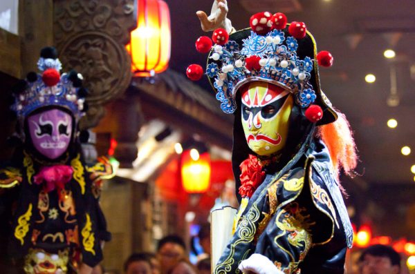 Traditional Chinese opera performance in Sichuan Province, China, with one performer wearing a yellow mask and the other performer wearing a purple one.