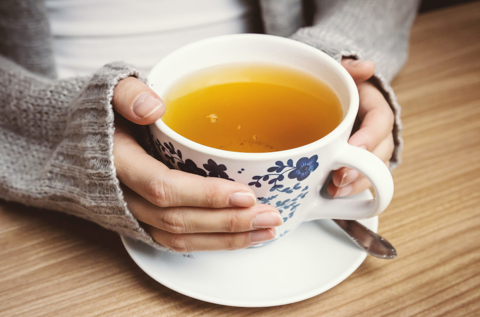 Female hands holding a blue and white porcelain cup filled with tea.