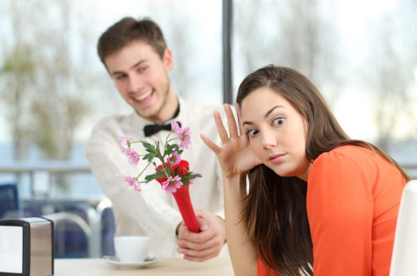 Young woman disgusted by a geeky boy handing her flowers.