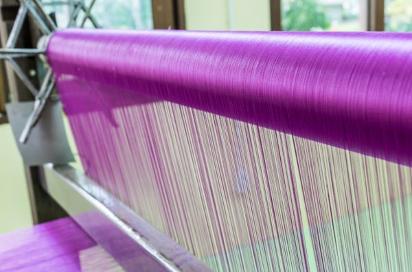 Silk weaving – Purple silk threads being woven on a loom.