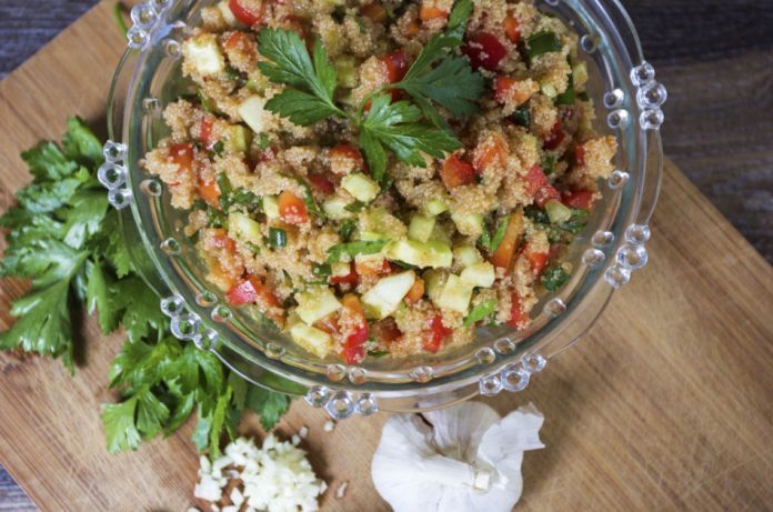 Amaranth salad with cucumbers and peppers in a clear bowl sitting on a wooden cutting board with a head of garlic and some cilantro.