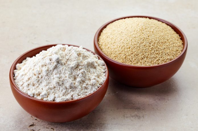 A bowl containing amaranth seeds sits next to a bowl containing amaranth flour.