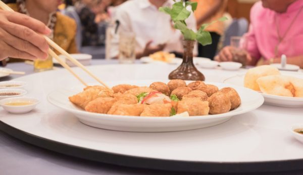 Fried food on dining table with hand holding chopsticks to pick it up in a restaurant.