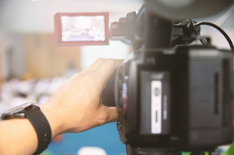 News camera seen from the rear with an Asian man's hand making some adjustments.