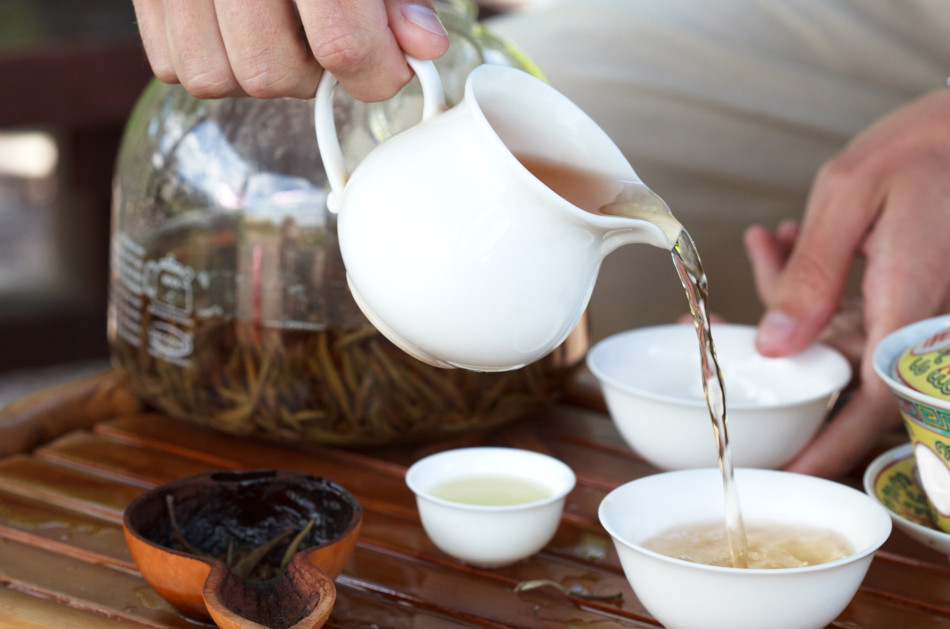 Traditional Chinese tea ceremony with cups and strainer on the table while a woman pours tea.
