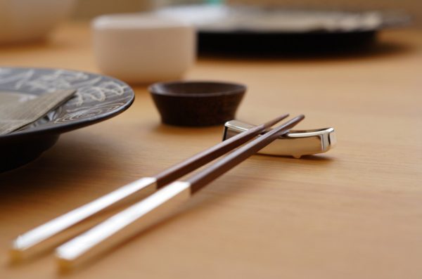 Wooden chopsticks resting on a chrome holder at a place setting at the dinner table.
