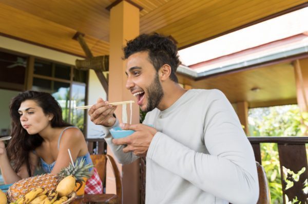Cheerful people tasting Asian noodles eating with chopsticks together.