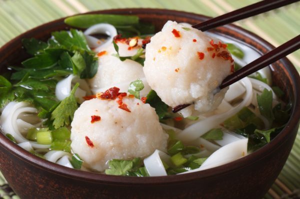 Traditional Asian soup with fish balls being eaten with chopsticks.