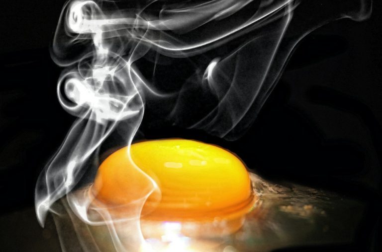 Closeup of an egg yolk frying in a pan.