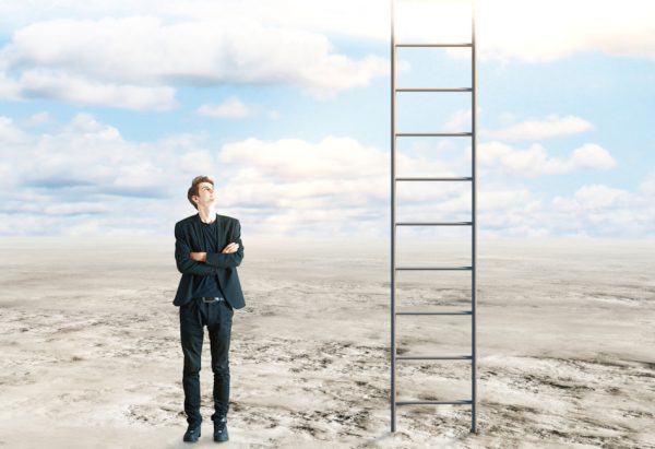Success and growth concept: Young businessman with folded arms standing in desert and looking up at ladder leading to the sky.