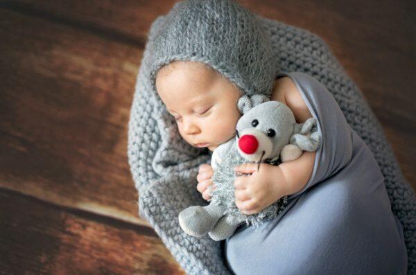 Little newborn baby boy sleeping in a bassinet holding a stuffed animal.