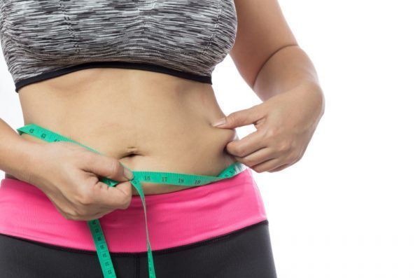Overweight woman uses a measuring tape to check her waist size.