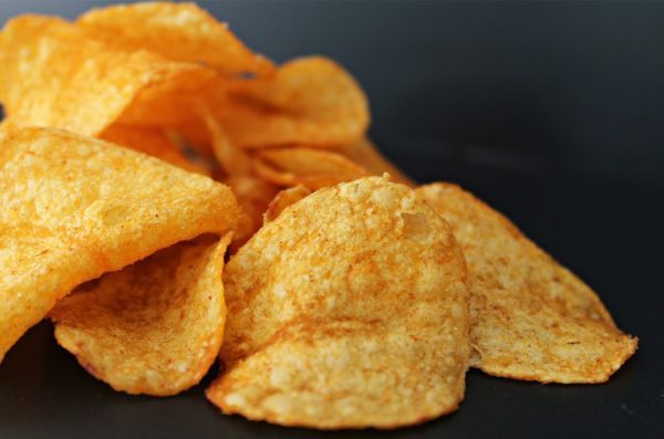A handful of potato chips sit on a dark countertop.