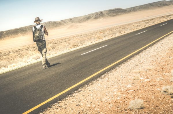 Man with a backpack walking on the road through the Namib Desert in Africa.
