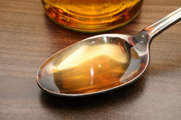 A bottle of apple cider vinegar with a spoonful of vinegar sitting in front of it.