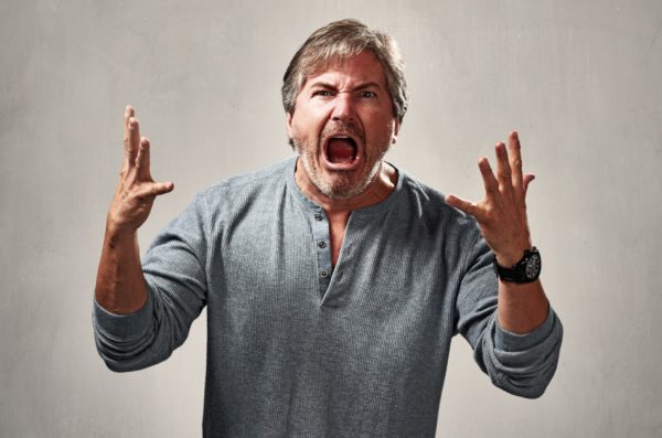 Man in gray shirt has both hands raised, yelling in an aggressive manner.