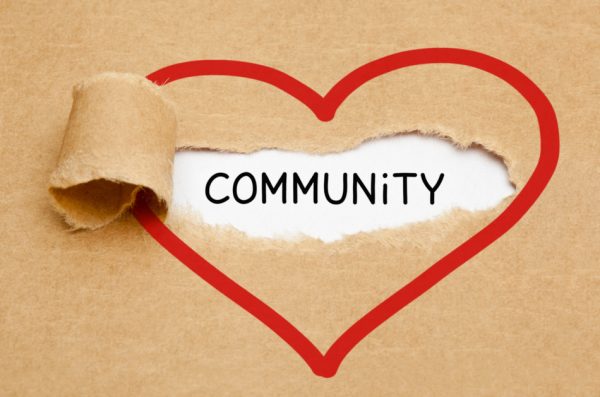Handwritten word "Community" appearing in a red hand-drawn heart behind torn brown paper.