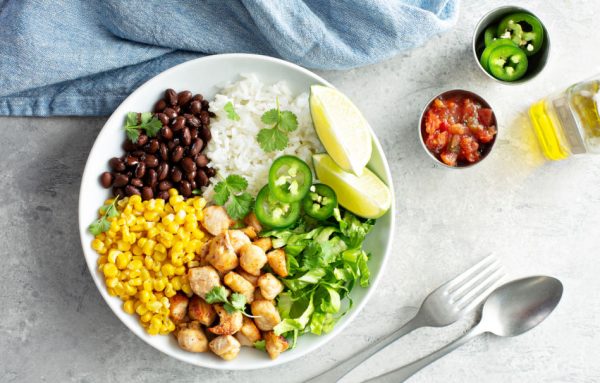 Chipotle spicy chicken lunch bowl with rice corn, beans, lettuce, jalapenos, and lime wedges.