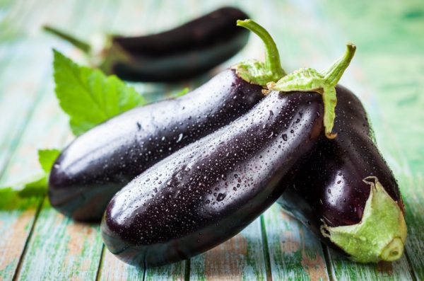 Four eggplants sitting on an old wooden table.
